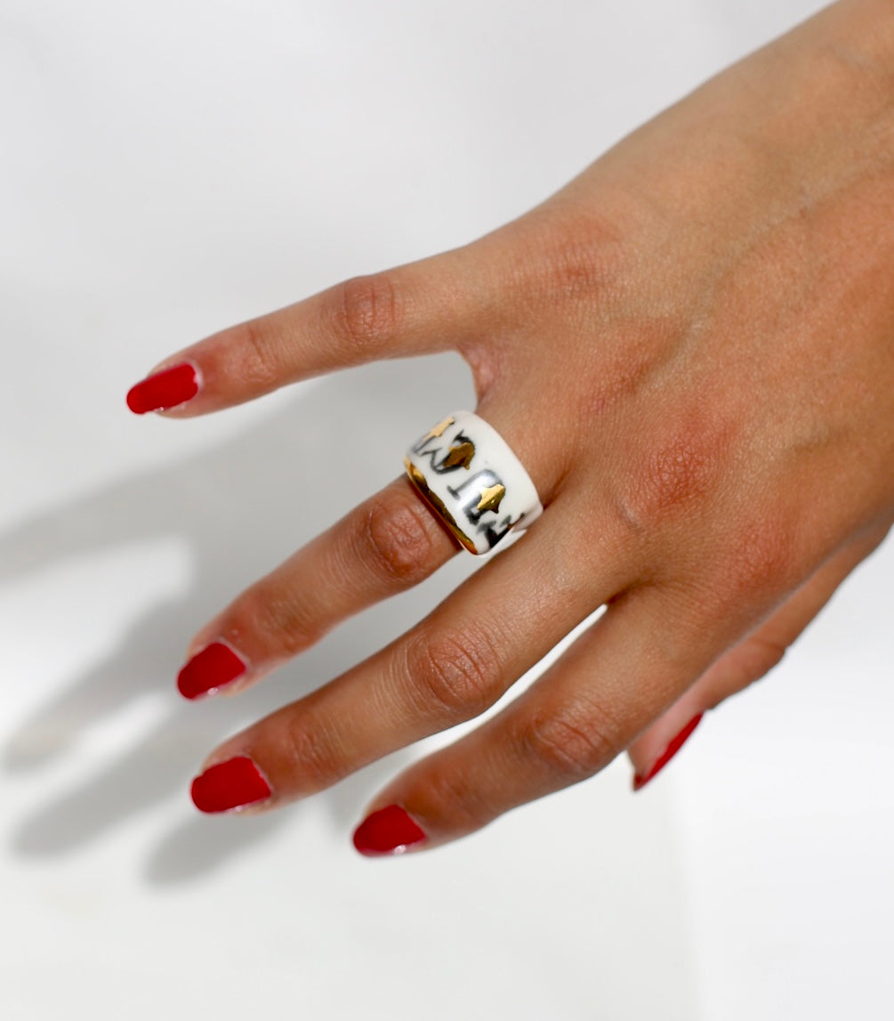 Bague type bandeau en porcelaine blanche émaillée en taille 53 FR avec un message FUCK ornées de petits motifs d'étoiles en or liquide peintes à la main.
