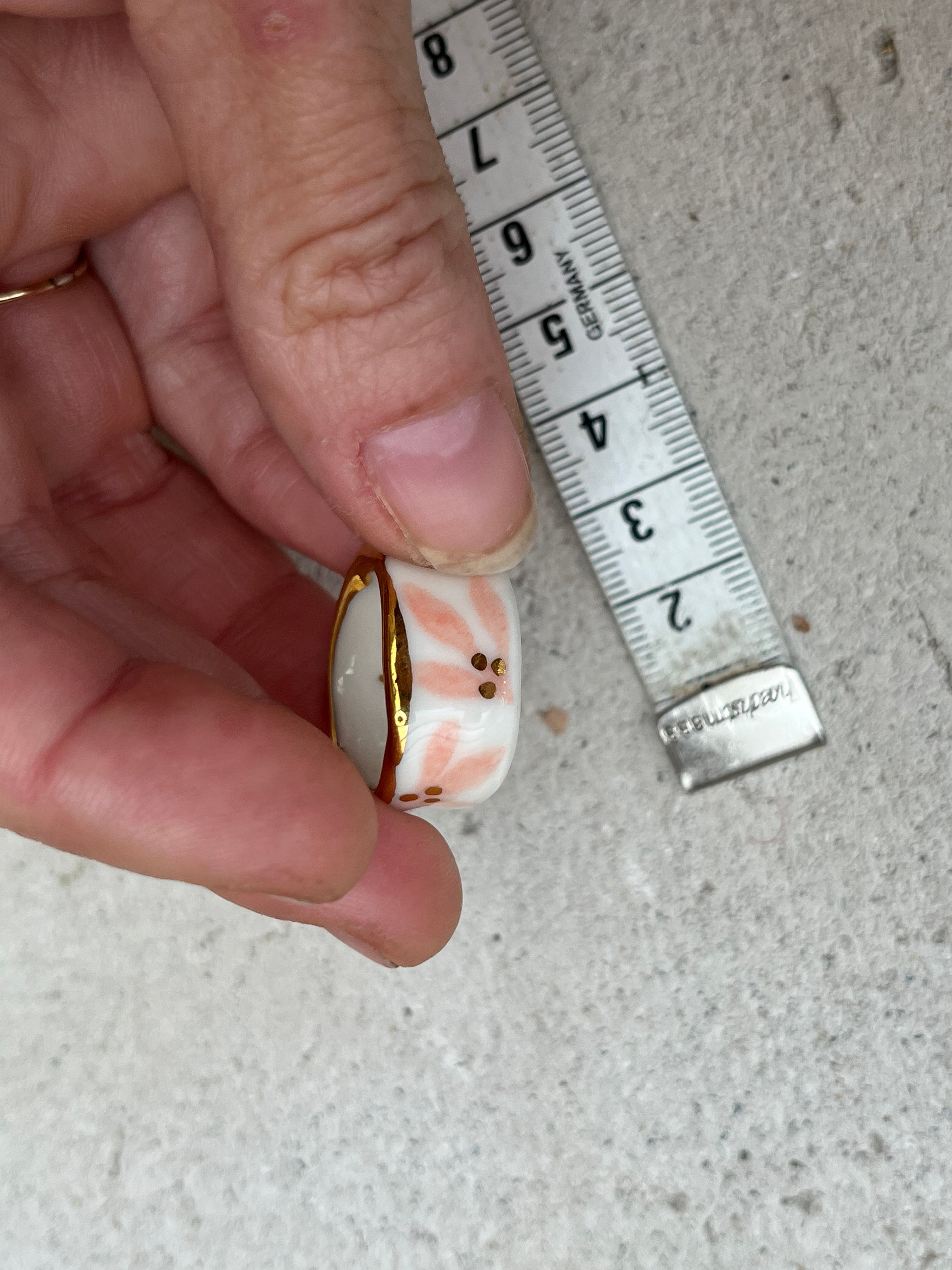bague en porcelaine blanche émaillée en taille 53 Fr, à motif fleurs rose et de points à l'or liquide fait à la main avec un liseré doré sur sa tranche.