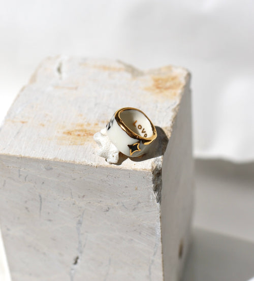 Bague large type bandeau en porcelaine blanche émaillée en taille 53 FR avec un message FUCK ornées de petits motifs d'étoiles en or liquide peintes à la main.