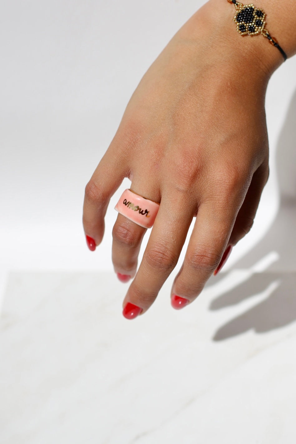 bague de type bandeau en porcelaine rose émaillée en taille 52 FR avec une inscription "amour" écrite ainsi qu'un œil protecteur dessiné à la main à l'or liquide.