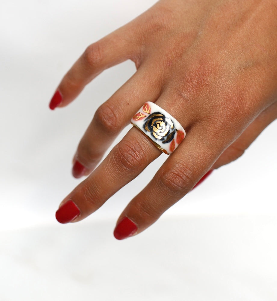 Une bague en porcelaine blanche émaillée en taille 51. Avec un motif rose noire stylisée peinte à l'or liquide avec des feuilles colorées. Avec une inscription  cachée "LOVE" en lettres dorées. Réalisée à la main à Lyon. 