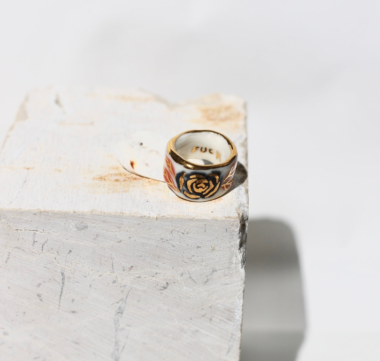 Une bague en porcelaine blanche émaillée en taille 51. Avec un motif rose noire stylisée peinte à l'or liquide avec des feuilles colorées. Avec une inscription  cachée "FUCK" en lettres dorées. Réalisée à la main à Lyon. 