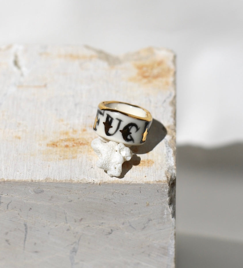 Bague large type bandeau en porcelaine blanche émaillée en taille 53 FR avec un message FUCK ornées de petits motifs d'étoiles en or liquide peintes à la main.