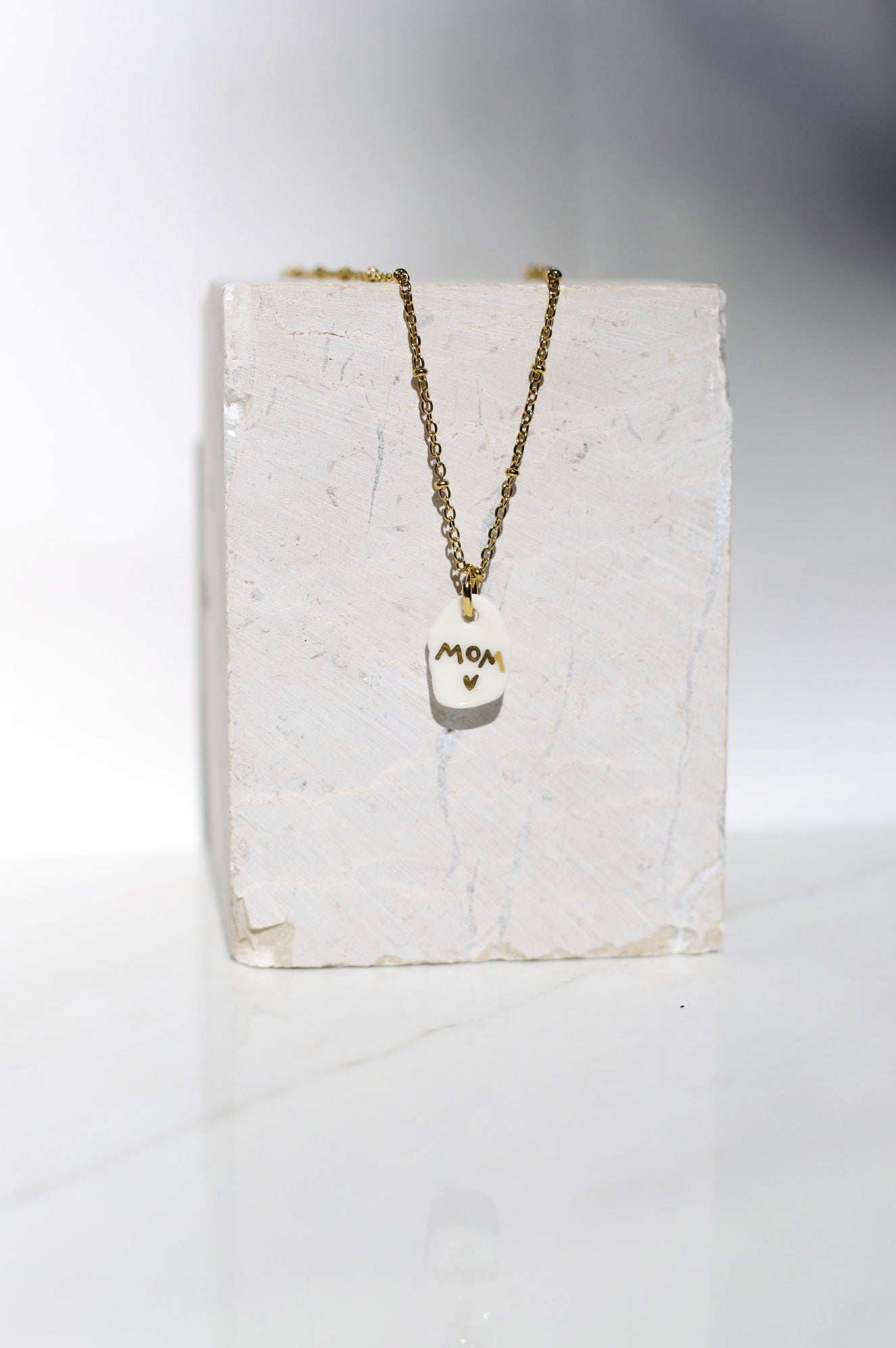 Bijoux de collier en porcelaine fabriqué à la main arborant le mot MOM avec des détails à l'or liquide 
