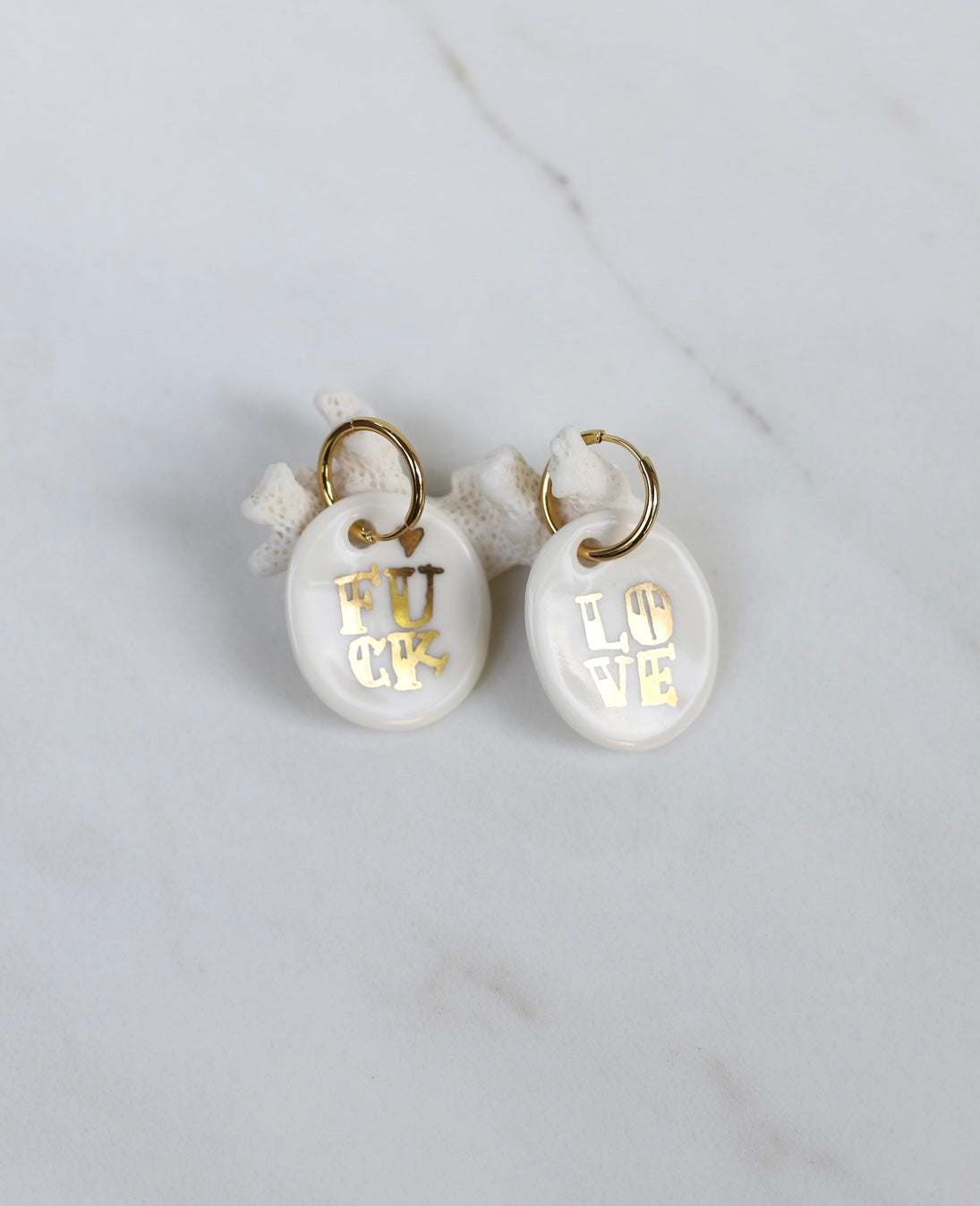 paire de boucles d'oreilles en porcelaine blanche, l'un portant l'inscription dorée LOVE et l'autre l'inscription dorée FUCK. Faites et peint à la main. 