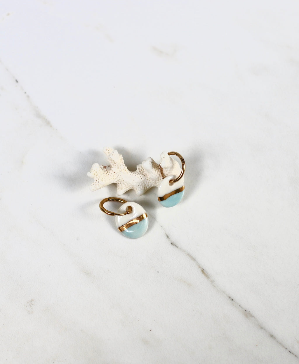 boucle d'oreille pendante dorée munie d'un petit pendentif rond en porcelaine bicolore blanche et bleu ciel, séparé au centre par une large bande d'or fin.