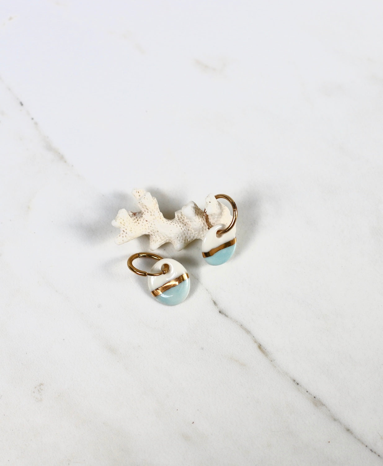 boucle d'oreille pendante dorée munie d'un petit pendentif rond en porcelaine bicolore blanche et bleu ciel, séparé au centre par une large bande d'or fin.
