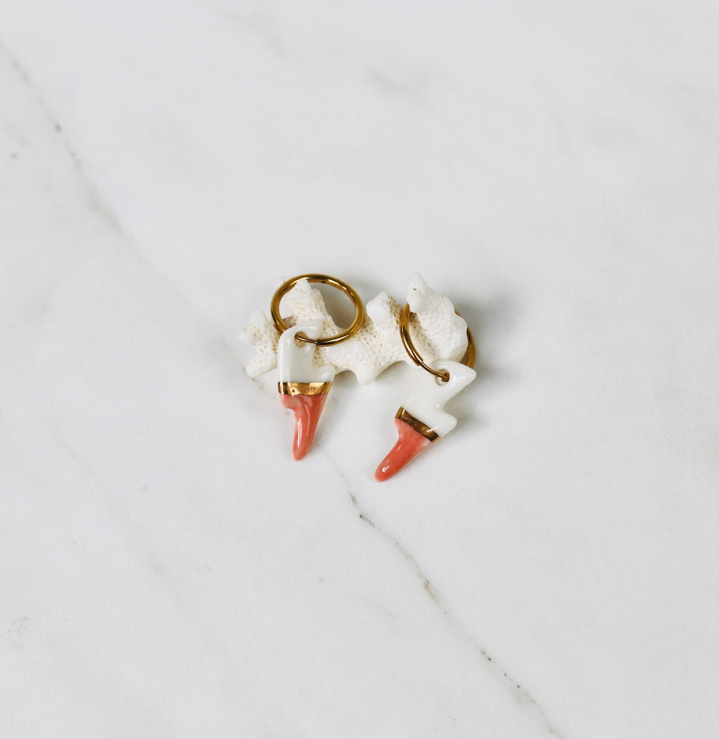 Une paire de boucles d'oreilles mini avec des pendentifs en forme d'éclair en porcelaine bicolore blanche et rose saumon, séparés par une ligne d'or fin.