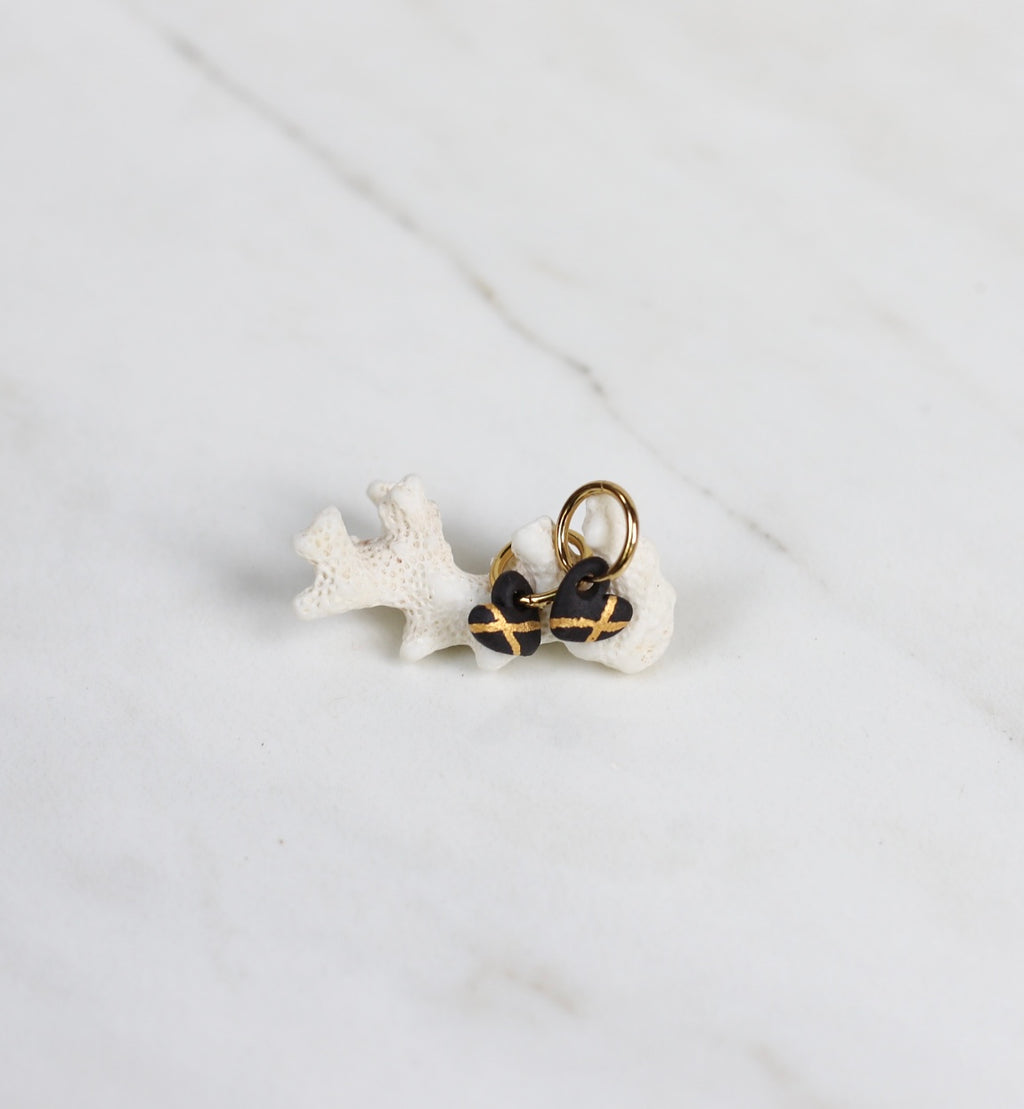 Paire de boucles d'oreilles mini avec petits pendentifs en forme de cœur sculpté en porcelaine noire mate, avec des lignes croisées peintes à la main à l'or brillant.