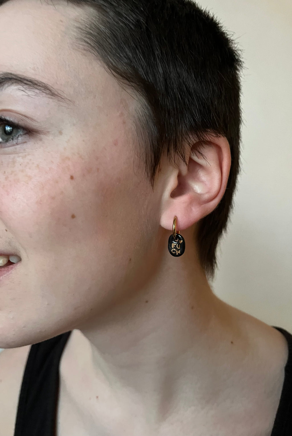 Boucle d'oreille rock en porcelaine noire et or portée à l'oreille, affichant le mot FUCK écrit à la main en lettres d'or liquide