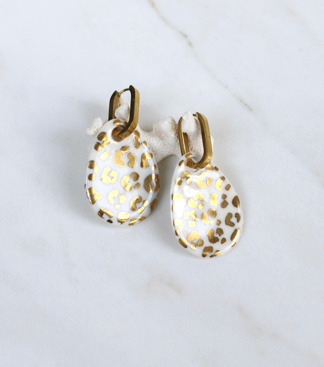 Paire de boucles d'oreilles pendantes en en porcelaine blanche émaillée, ornées de taches léopard peintes à l'or fin liquide.