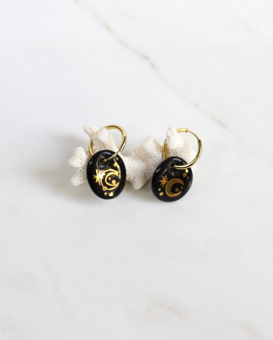 Paire de boucles d'oreilles mini dorées ornées de pendentifs porcelaine émaillée, avec un motif de lune peint à la main et sublimé de finitions d'or peint à la main. 