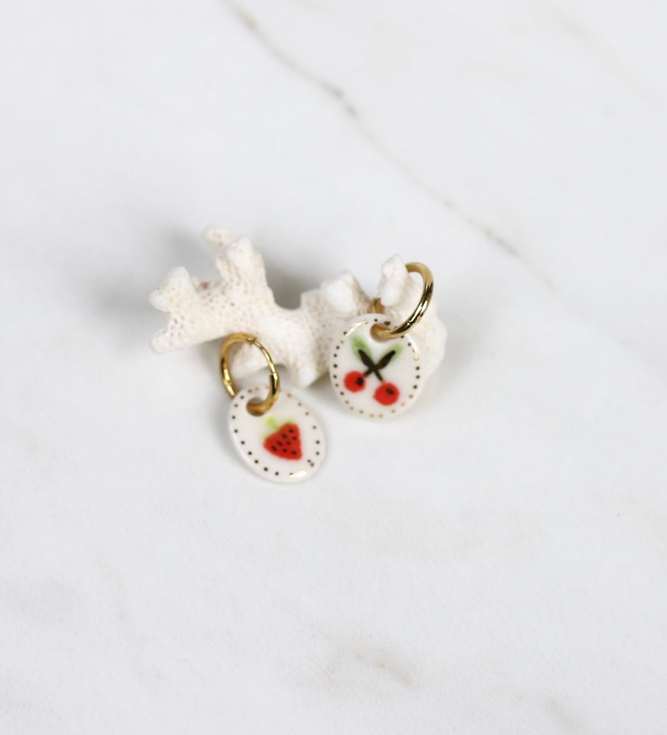 La fraîcheur d’une paire de boucles dépareillée en porcelaine, avec une fraise et des cerises dessinées 