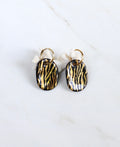 paire de boucles d'oreilles dorées avec des pendentifs de forme ovale en porcelaine noire ornés de rayures zébrées à l'or fin.