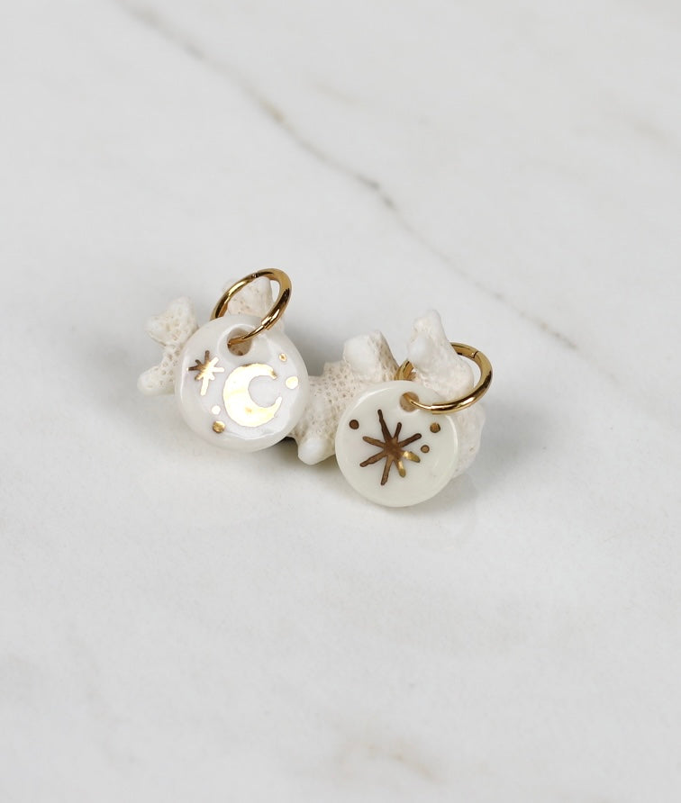 Paire de boucles d'oreilles pendantes dépareillée en porcelaine blanche, l'une orné d'un croissant de lune brillante et l'autre d'une étoile étincelante peinte à l'or fin à la main