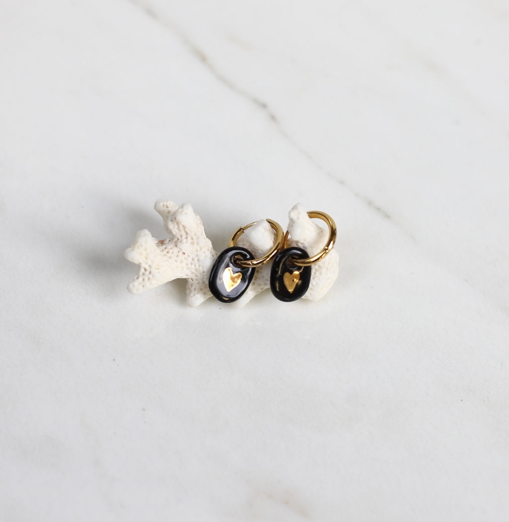 paire de boucles d'oreilles pendantes noir avec un motif coeur en or liquide dessinée à la main. 