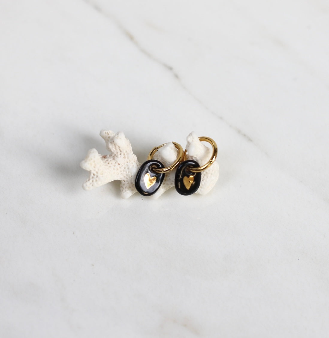 paire de boucles d'oreilles pendantes noir avec un motif coeur en or liquide dessinée à la main. 