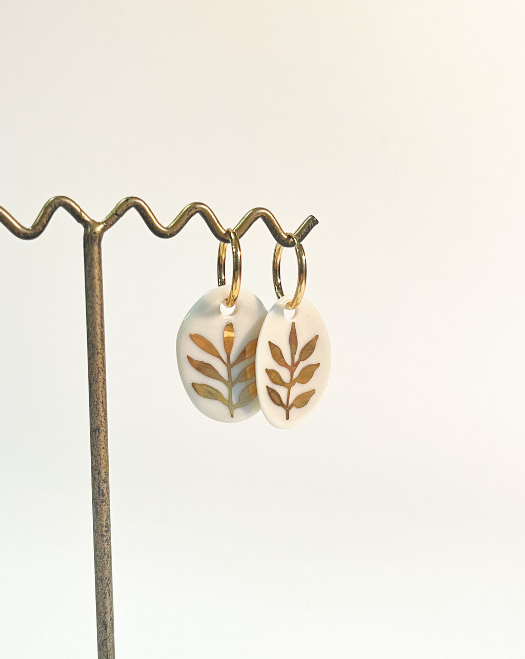 paire de boucles d'oreilles en porcelaine blanche ornées de feuilles dorées peintes à la main. Bijoux uniques de créateur français
