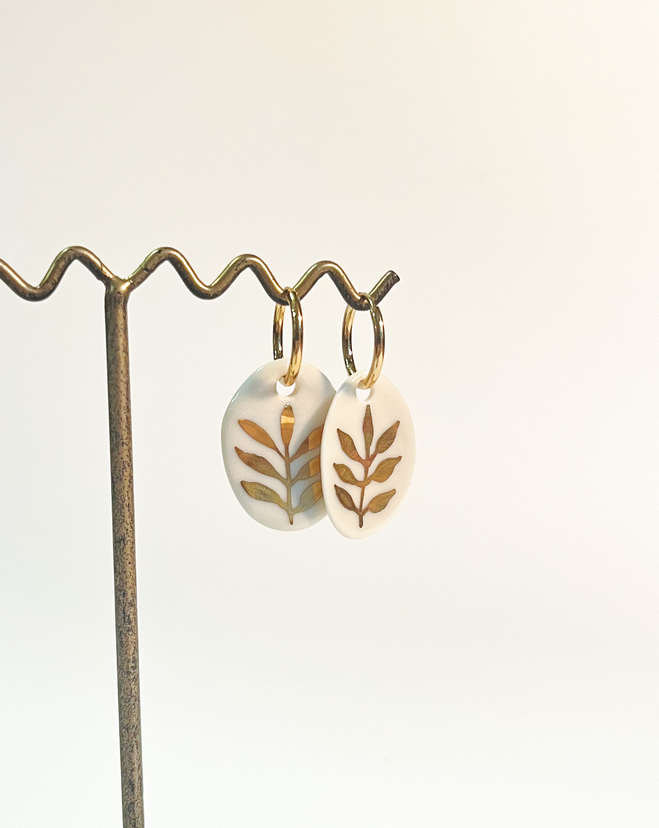 paire de boucles d'oreilles en porcelaine blanche ornées de feuilles dorées peintes à la main. Bijoux uniques de créateur français