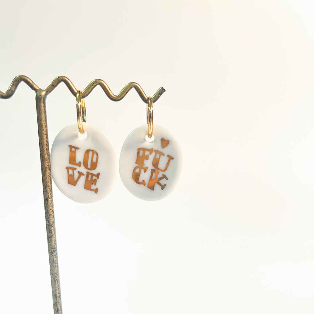 boucles d'oreilles avec charms en porcelaine blanche émaillée, affichant les mots LOVE et FUCK peints à l'or fin.