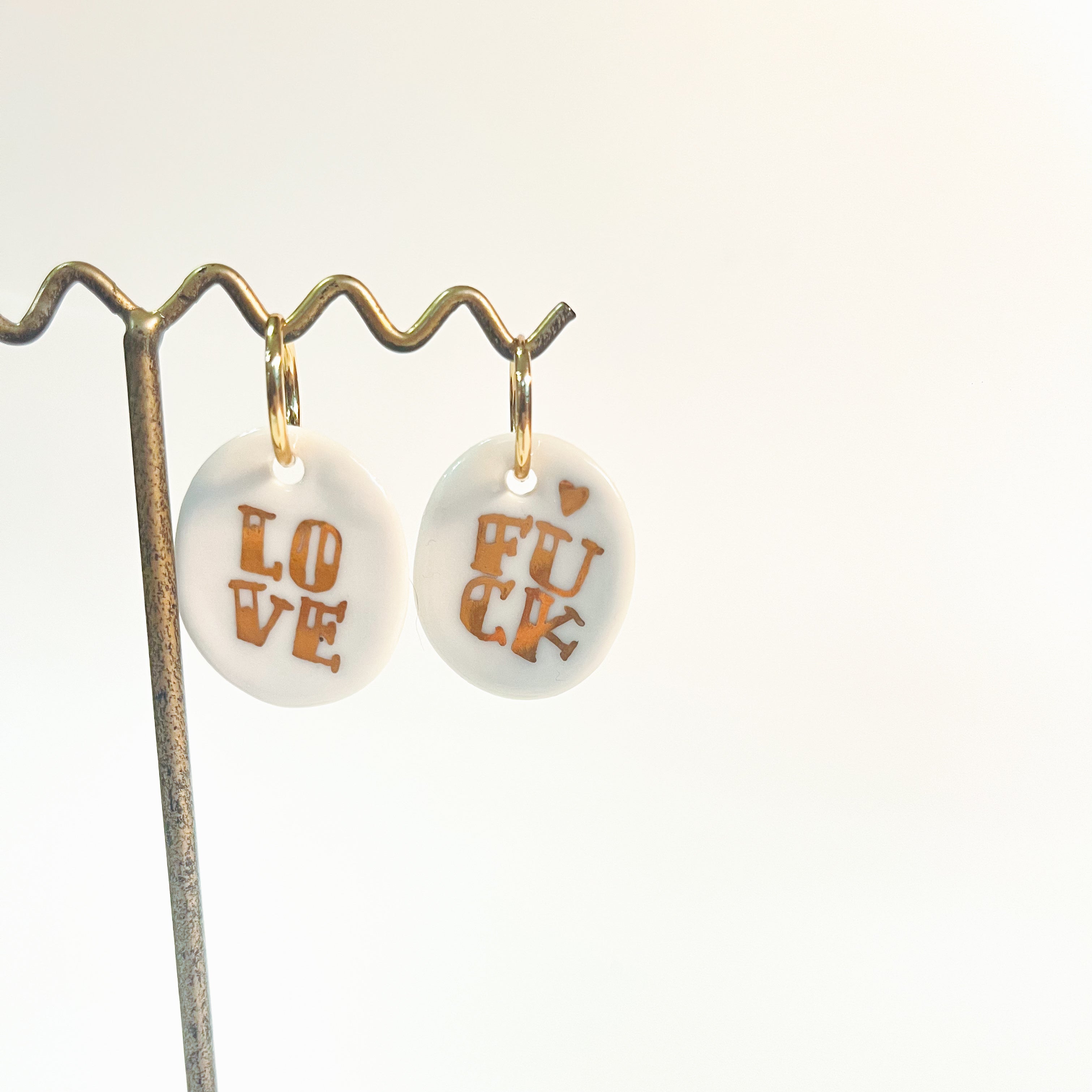 boucles d'oreilles avec charms en porcelaine blanche émaillée, affichant les mots LOVE et FUCK peints à l'or fin.