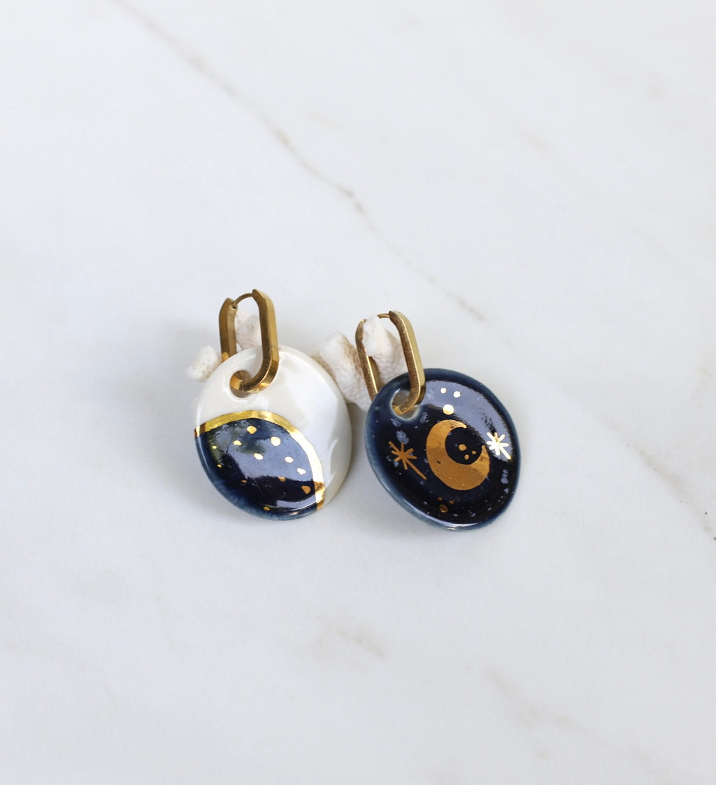 Une grande paire de boucles dépareillées en céramique, avec motif alchimie, lune et soleil bleu 