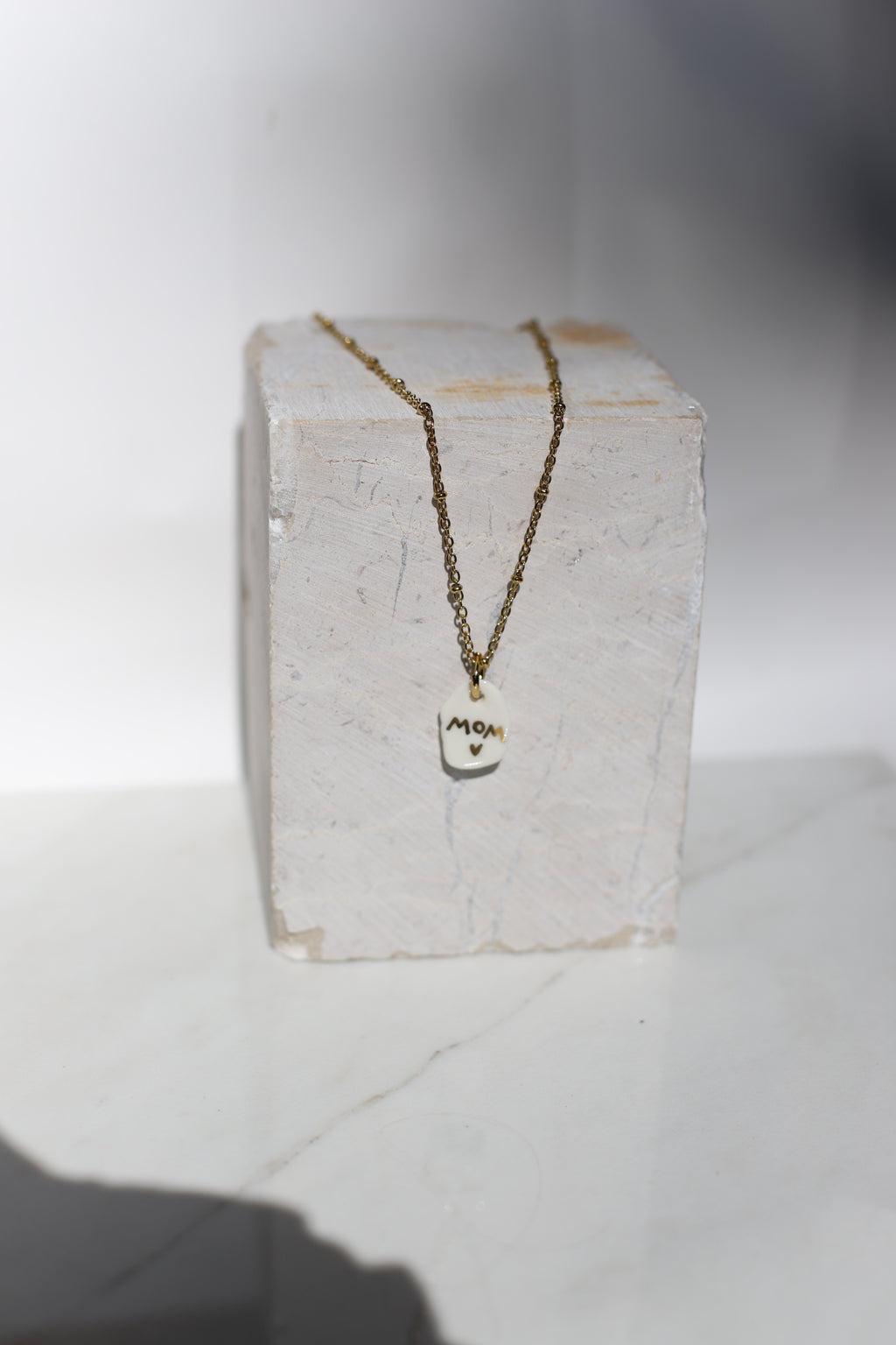 Bijoux en céramique pour les mamans avec un pendentif montrant le mot mom peint à l'or liquide 