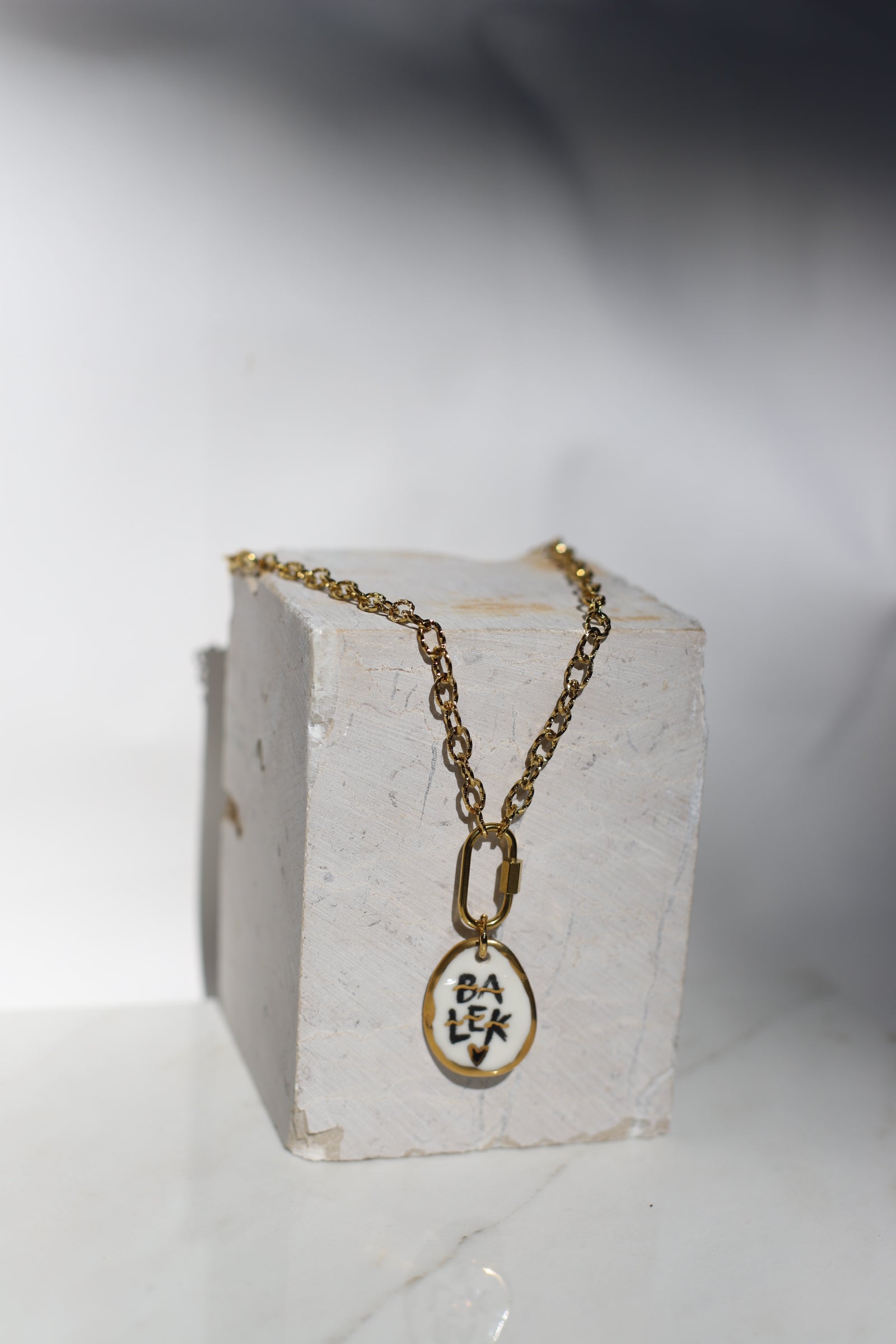 Collier en acier inoxydable avec des grosse chaîne et un médaillon en porcelaine fait à la main arborant le mot balek avec des détails à l'or peint à la main 