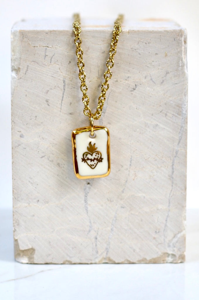 collier ex-voto doté avec un  pendentif  en porcelaine blanche émaillée, avec un motif cœur  aux flammes d'or et un liseré doré  sur les tranches peint à la main