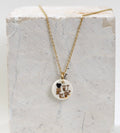 collier délicat composé d'une petite chaîne dorée et d'une médaille ronde en porcelaine blanche avec le mot FUCK écrit à l'or fin et un mini cœur noir.