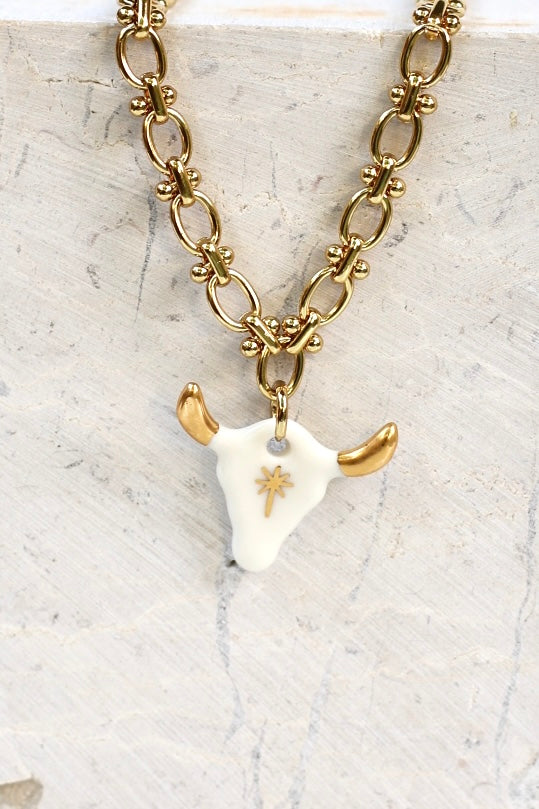 Le collier avec son pendentif tête de taureau blanc et or peint à la main chez Matilou.