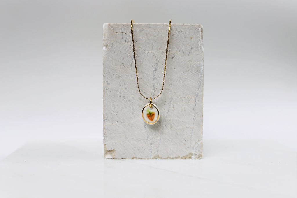 Collier fin doré orné d'un pendentif ovale en porcelaine blanche émaillée avec une  fraise peinte à la main, rehaussée d'un délicat liseré d'or. pendentif peint à la main 