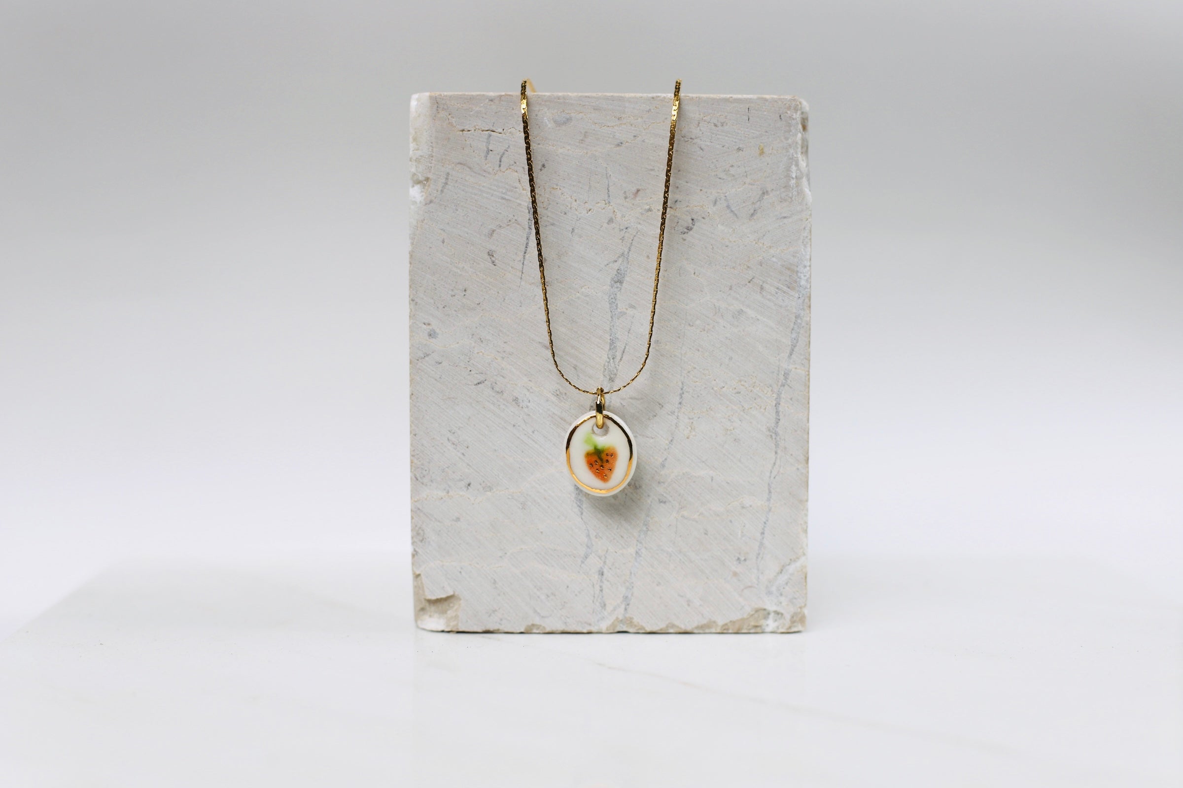 Collier fin doré orné d'un pendentif ovale en porcelaine blanche émaillée avec une  fraise peinte à la main, rehaussée d'un délicat liseré d'or. pendentif peint à la main 
