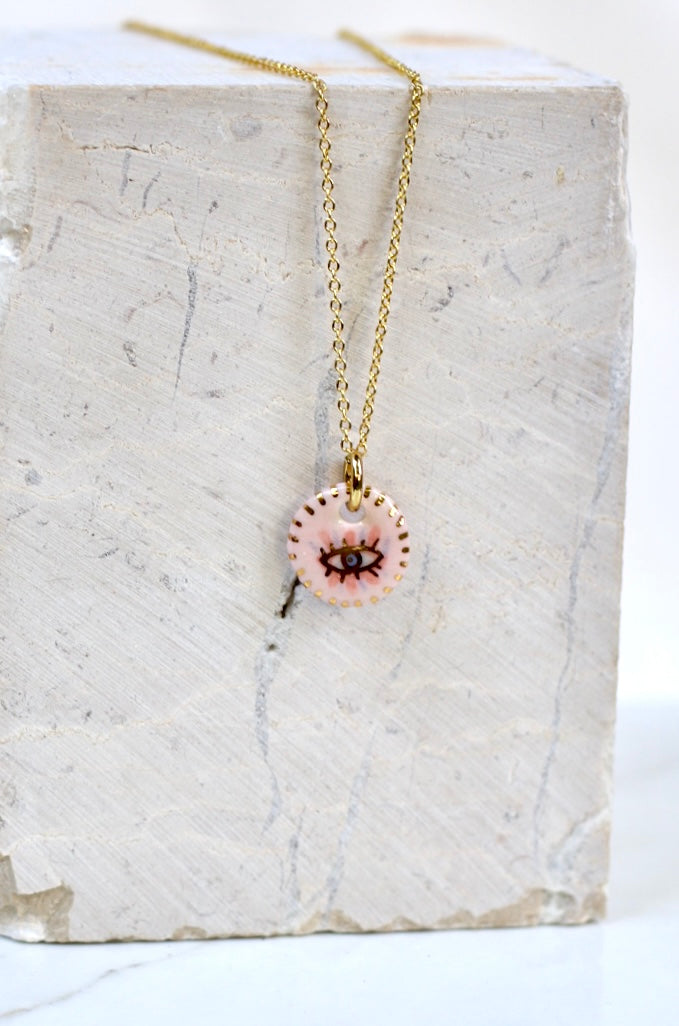 collier talisman orné d'un pendentif en porcelaine rose à motif œil de protection peint à la main avec des détails à l'or liquide
