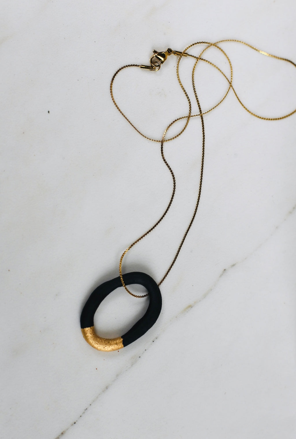 collier de créateur avec son pendentif créole en porcelaine noire, souligné par un épais liseré d'or étincelant appliqué à la main.