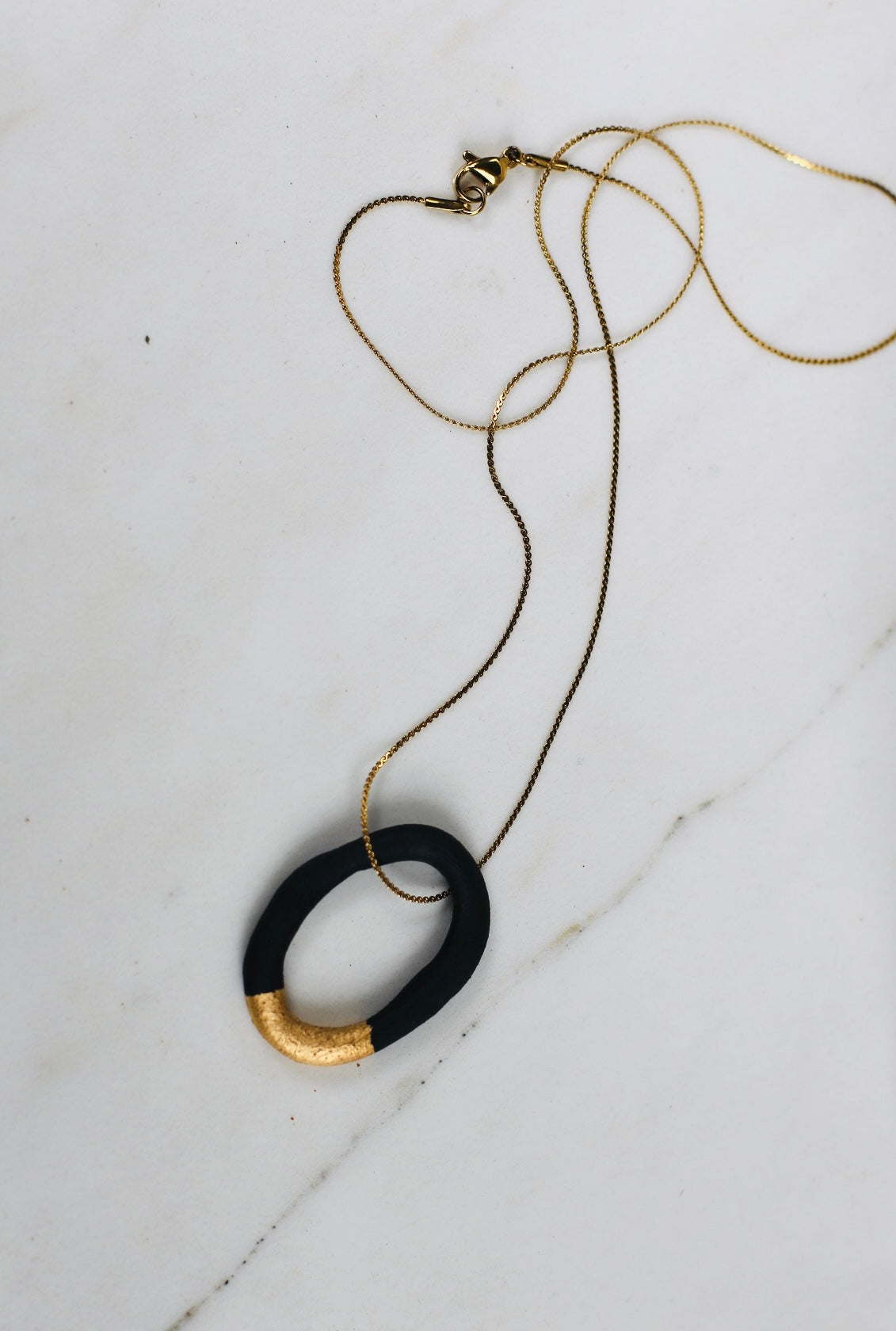 collier de créateur avec son pendentif créole en porcelaine noire, souligné par un épais liseré d'or étincelant appliqué à la main.