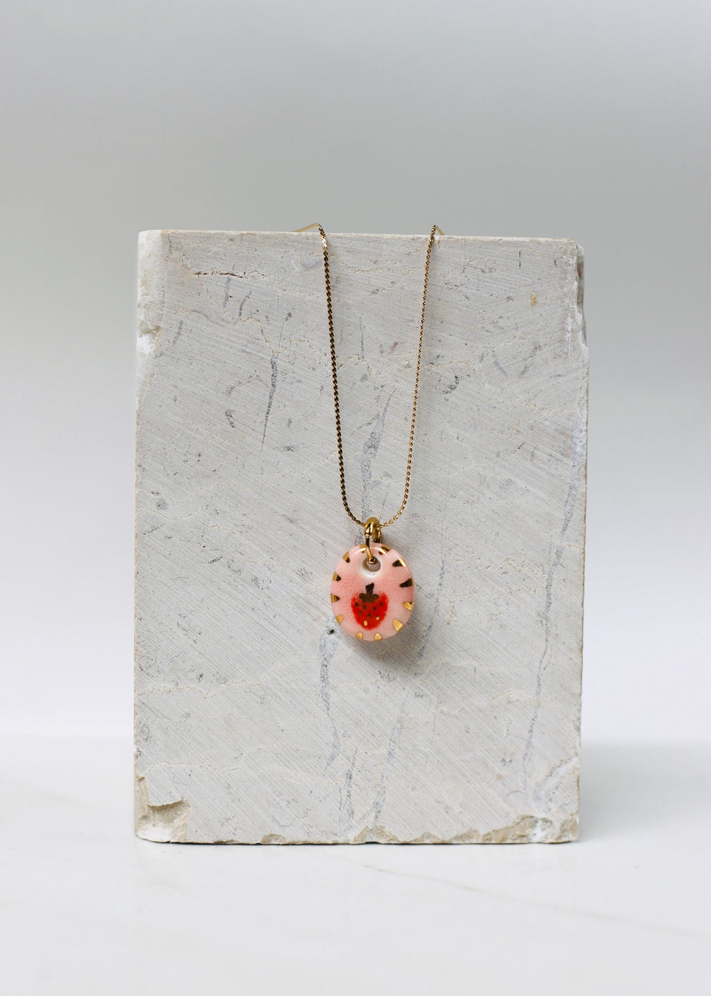 collier à motif fraise en porcelaine rose avec de petit détails dorés sur les bords peint à la main. 