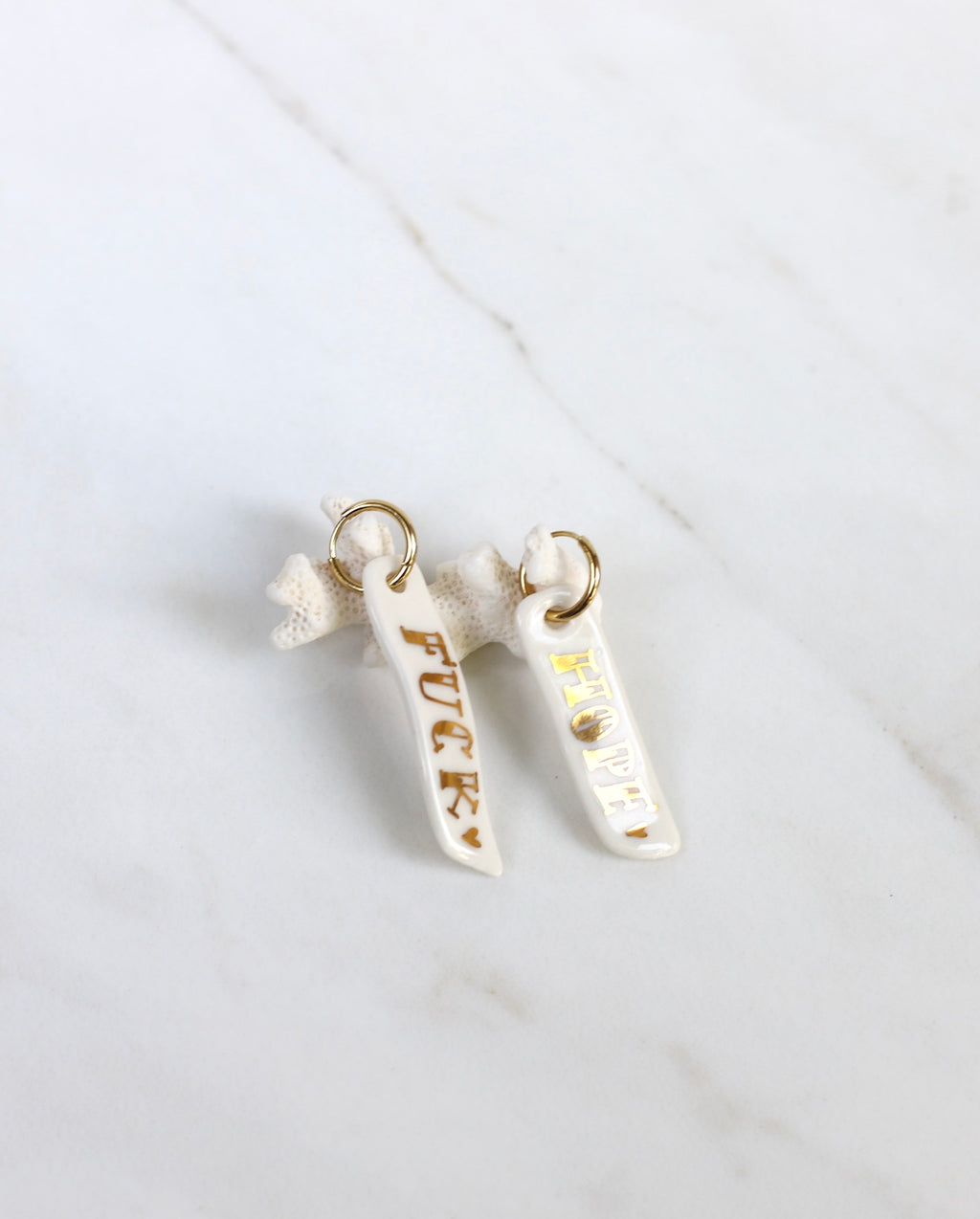 Paire de longues boucles d'oreilles pendantes asymétriques en porcelaine blanche pour femme. Barrettes verticales ornées des mots FUCK et HOPE écrits en lettres d'or fin avec un mini cœur doré