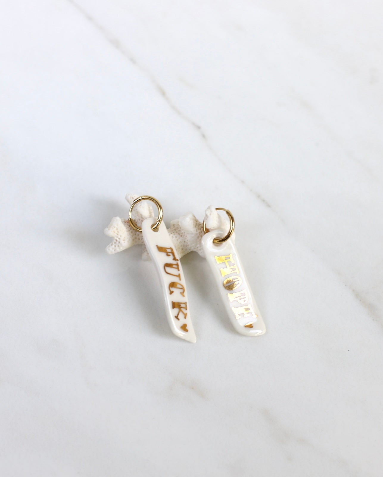 Paire de longues boucles d'oreilles pendantes asymétriques en porcelaine blanche pour femme. Barrettes verticales ornées des mots FUCK et HOPE écrits en lettres d'or fin avec un mini cœur doré