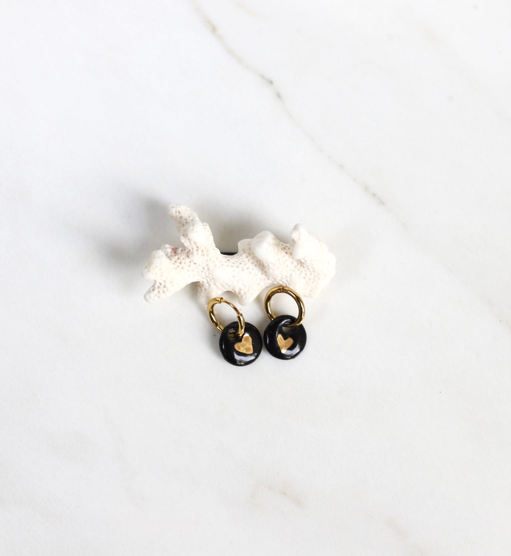 Paire de mini boucles d'oreilles pendantes pour femme. Petits motif ronds en porcelaine noire émaillée ornée d'un cœur or peint à la main.