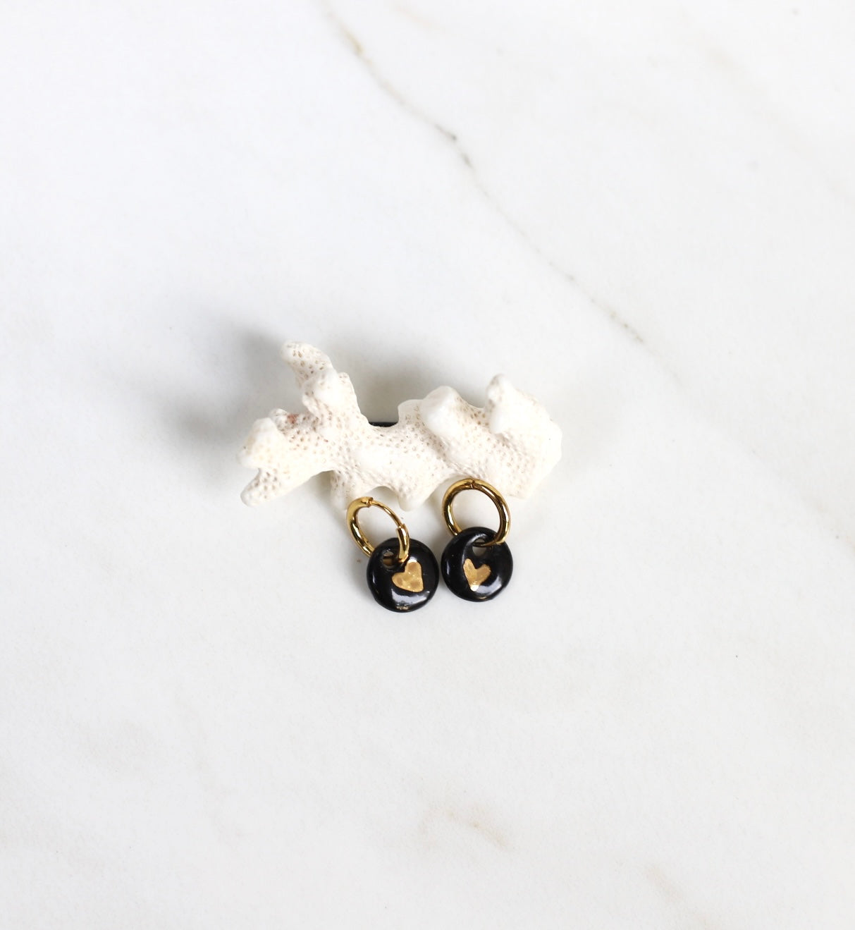 Paire de mini boucles d'oreilles pendantes pour femme. Petits motif ronds en porcelaine noire émaillée ornée d'un cœur or peint à la main.
