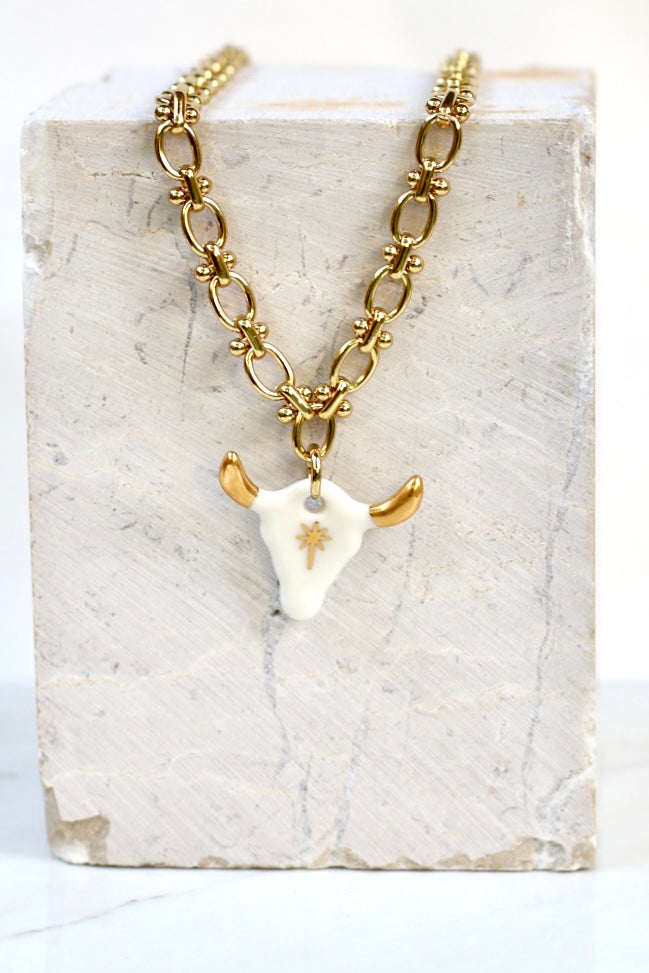 Collier Coachella composé d'un pendentif en porcelaine blanche en forme de tête de taureau orné de cornes à l'or précieux et d'une étoile centrale en or liquide peinte à la main.