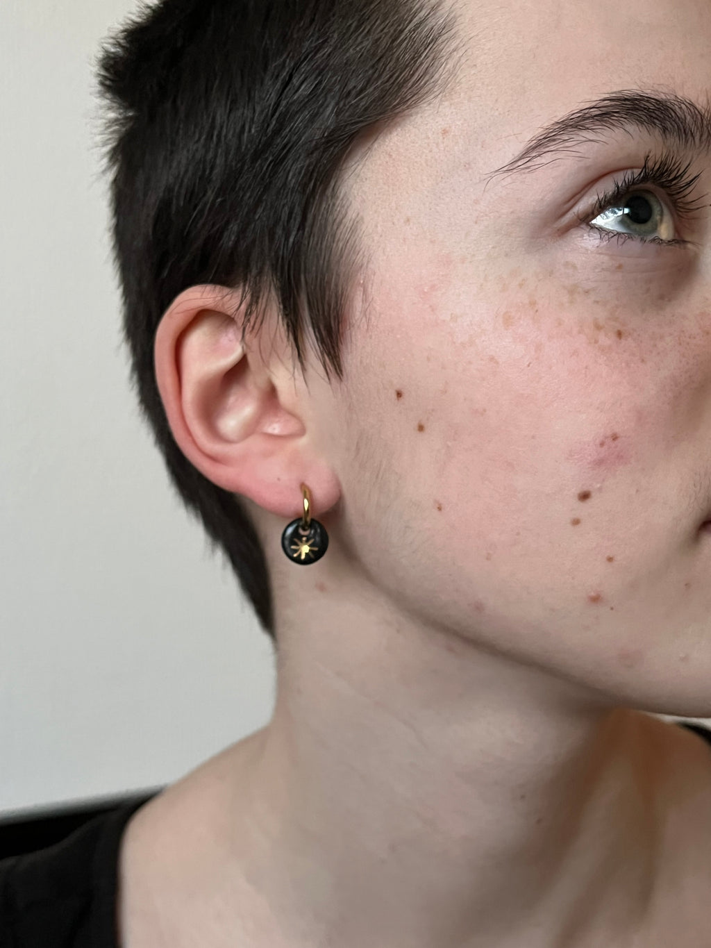 Petite boucle d'oreille en porcelaine noire ornée d'une étoile dorée éclatante, portée à l'oreille. Bijou de créateur fin et poétique pour femme