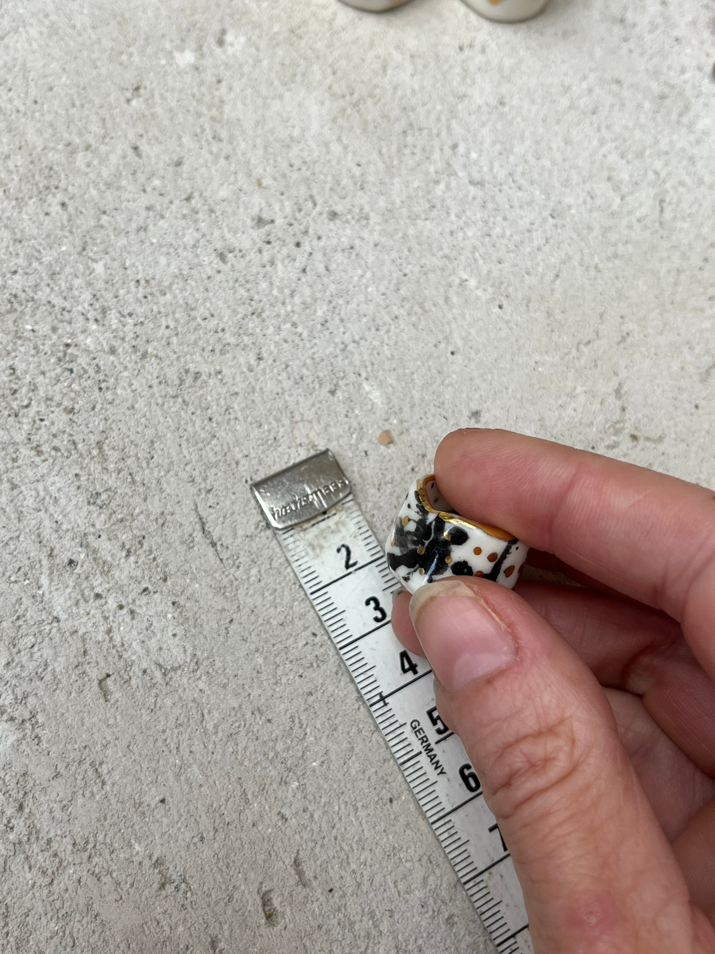 bague pour l'auriculaire en porcelaine émaillée blanche en taille 47 FR, avec un motif  abstrait de taches d'encre noires intenses et des touches d'or brillant.