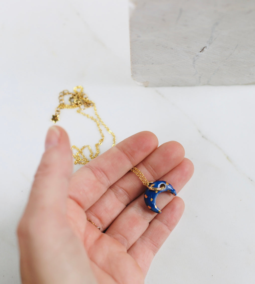 collier avec un médaillon en porcelaine émaillée avec un pendentif en forme de lune bleu nuit peinte et des détail à l'or peint à la main. Bijou de créatrice française 