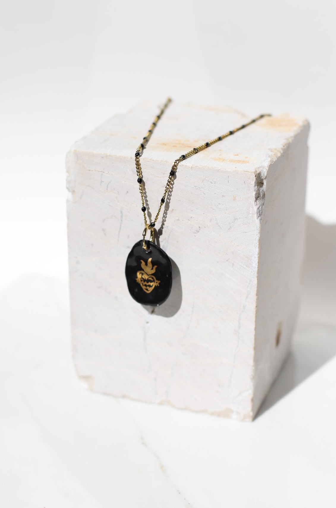 pendentif ovale asymétrique en porcelaine noire brillante rehaussé d'un cœur enflammé à l'or liquide fais main
