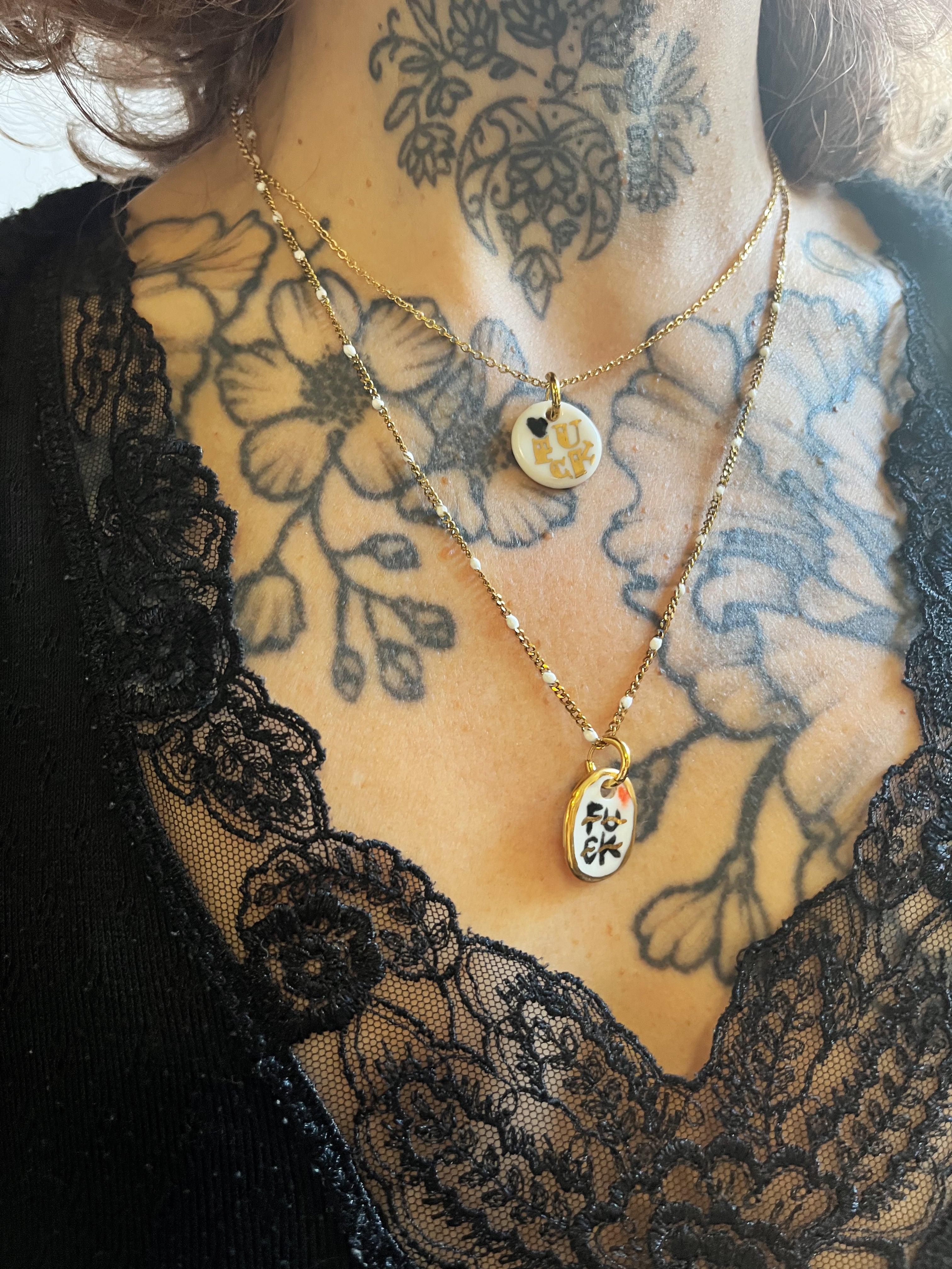 collier médaille ronde en porcelaine blanche ornée du mot FUCK peint à l'or fin liquide avec un mini cœur noir