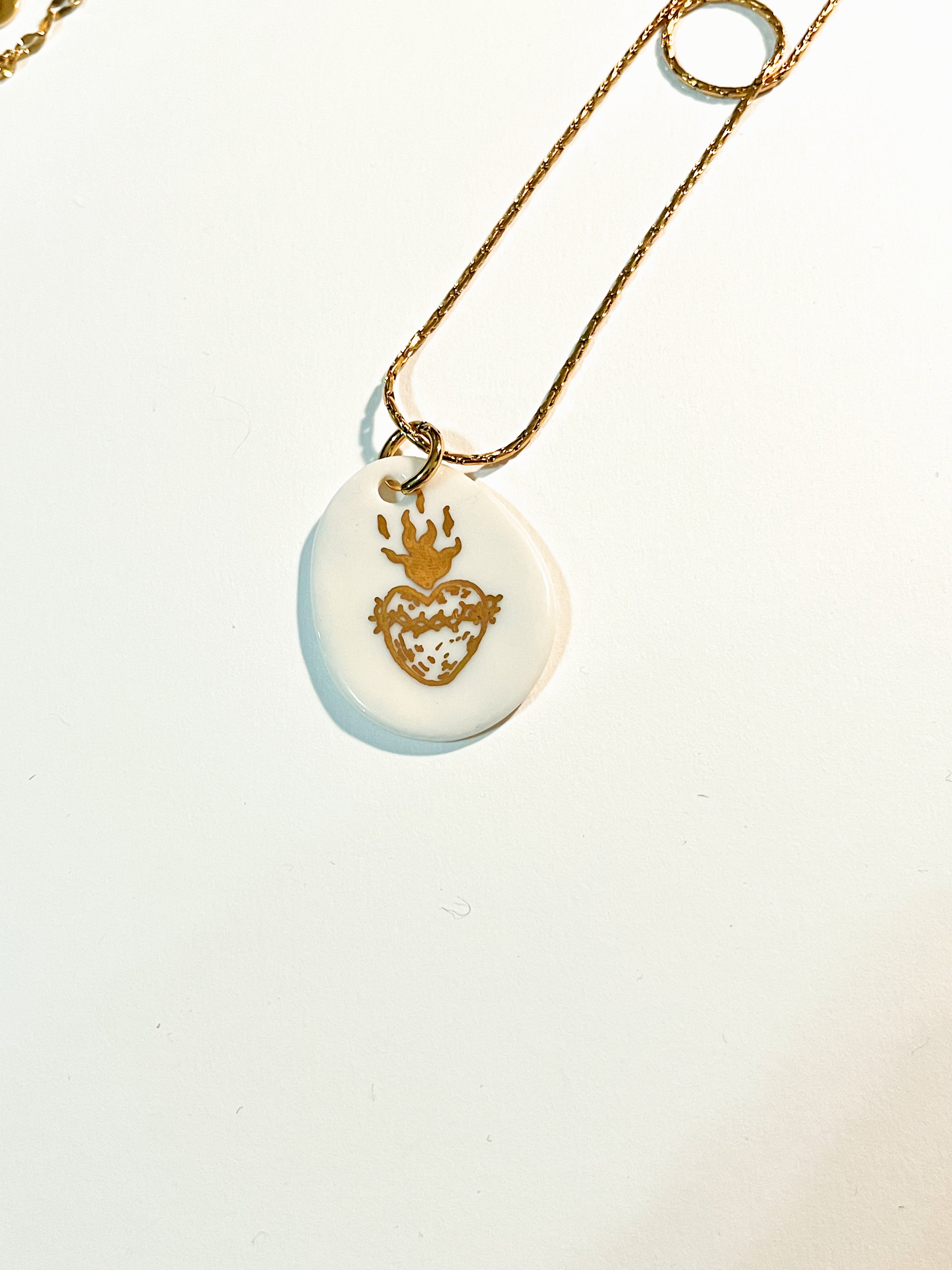 Vue détaillée d'une médaille ovale irrégulière en porcelaine véritable avec un cœur ex-voto et des flammes dessinés à l'or fin liquide.