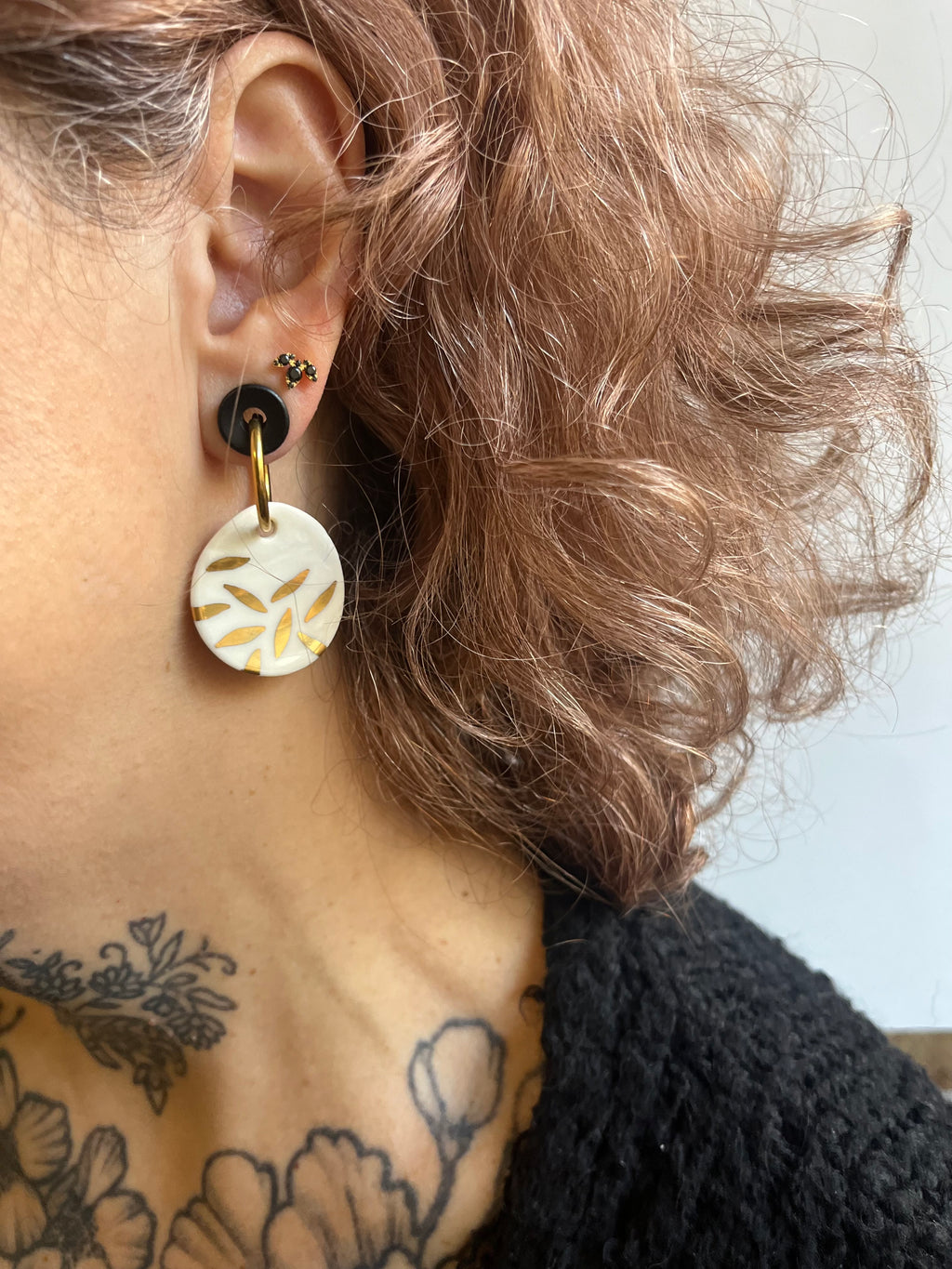 boucle d'oreille pendante en porcelaine, avec des éclats d'or sur le médaillon blanc.