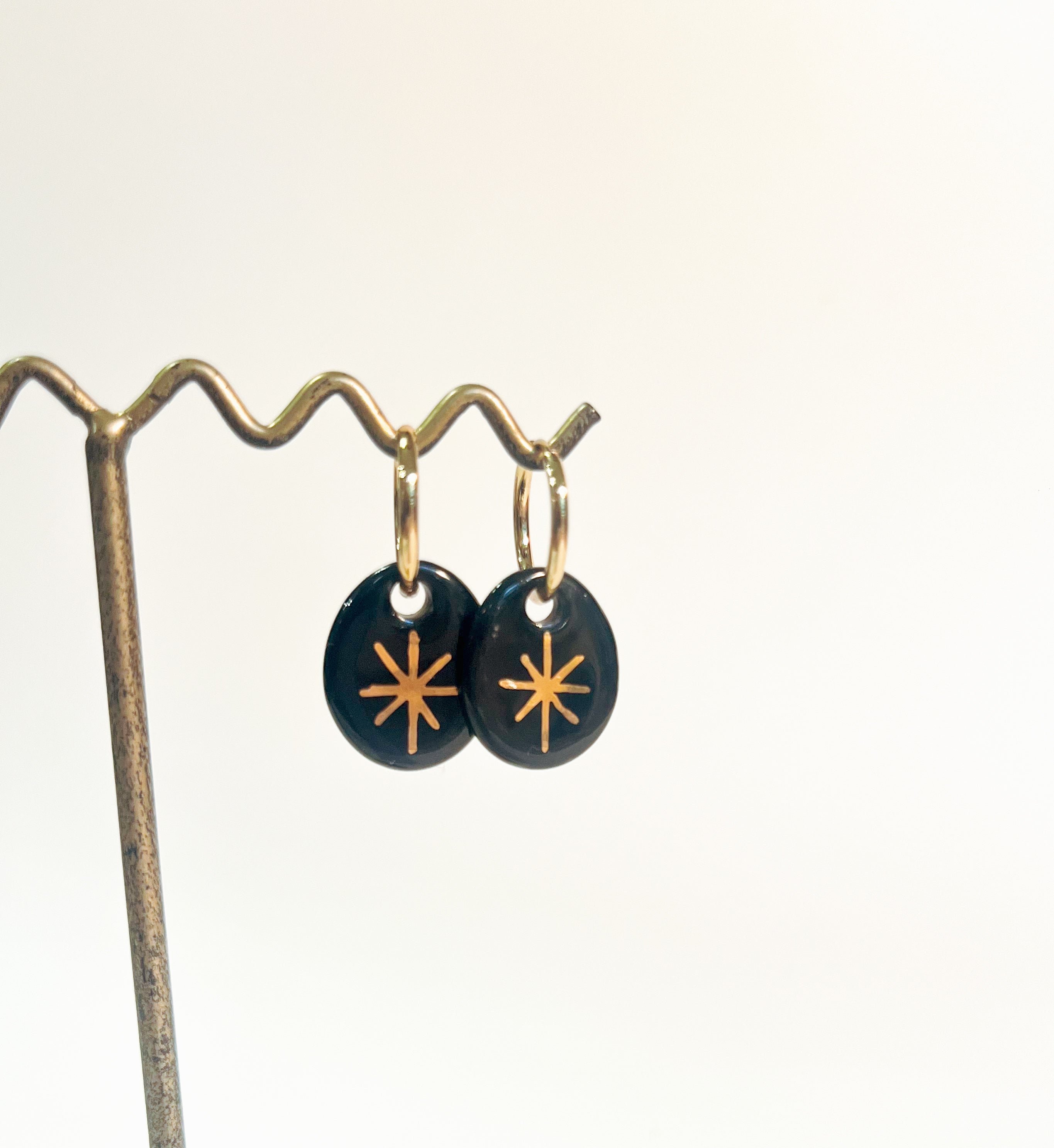 boucle d'oreille dorée avec son pendentif en porcelaine noir affichant une étoile dorée brillante faites à la main 